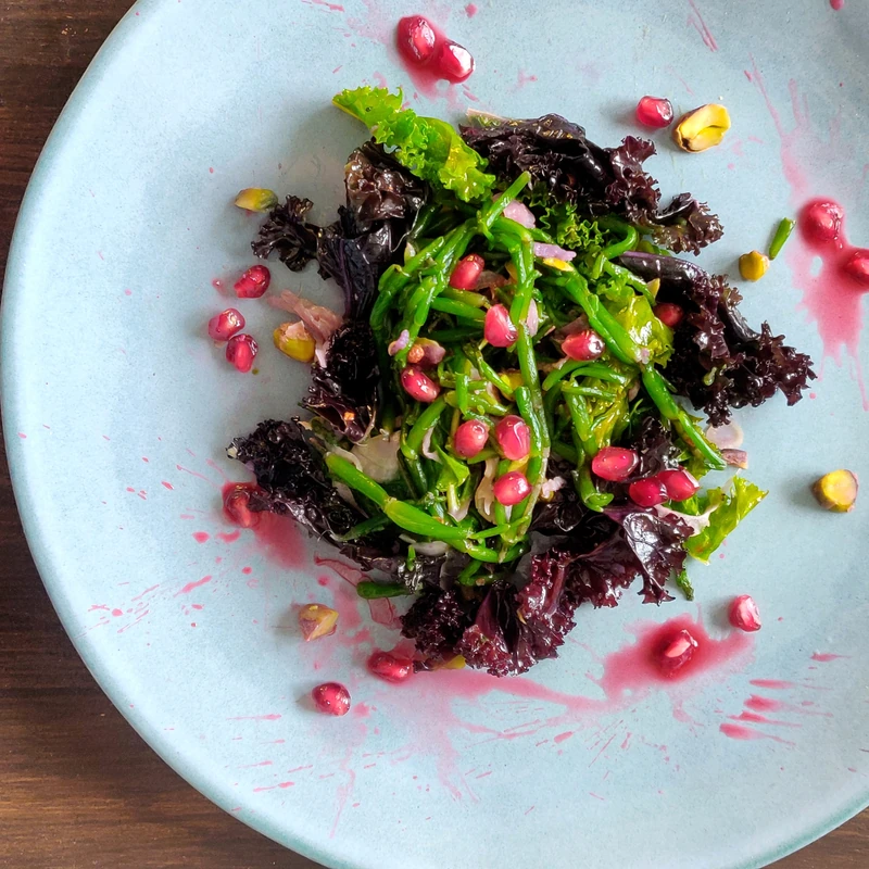 Salade verte, salicorne, grenade et pistaches dans une assiette bleue