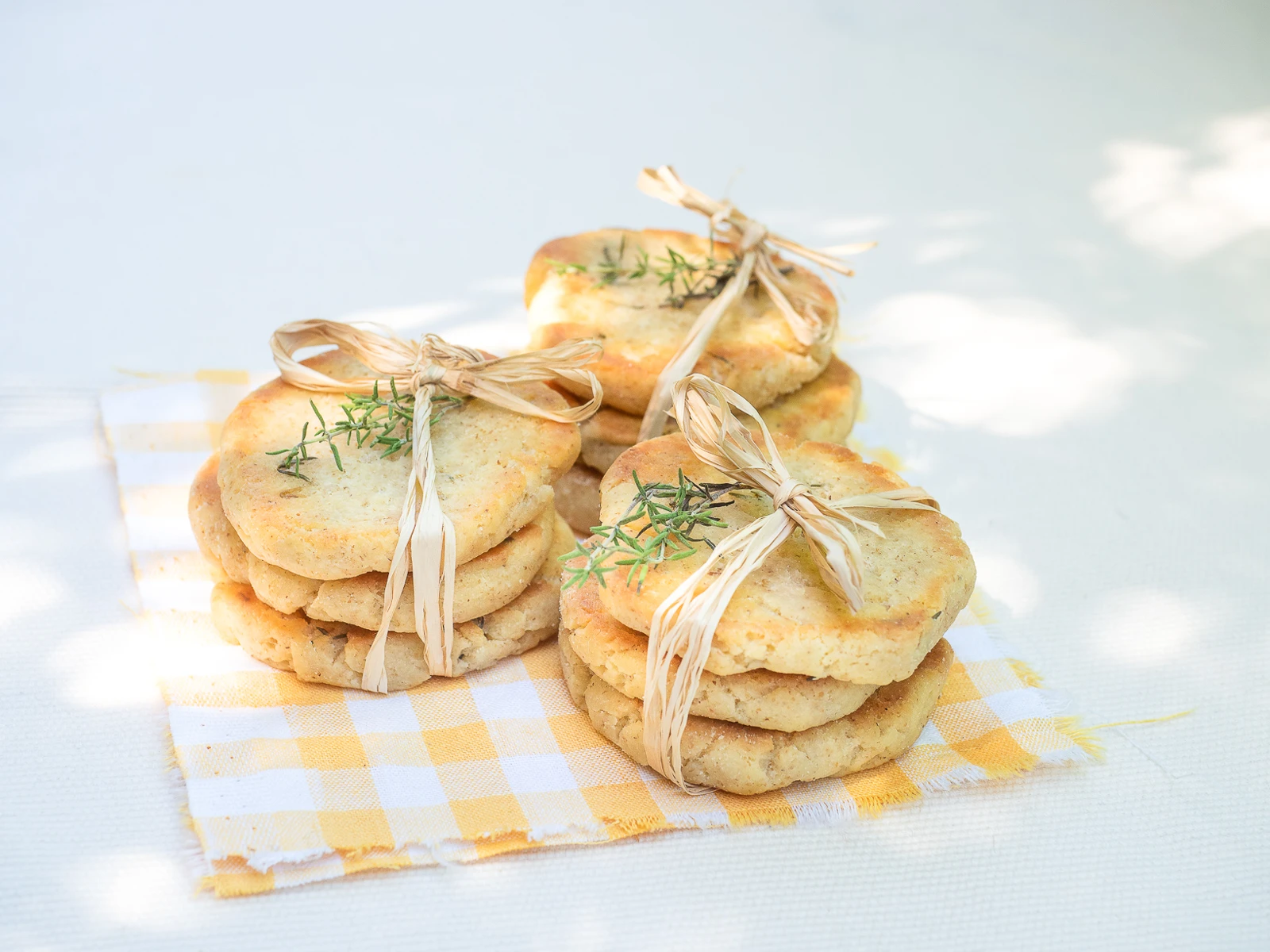 Biscuits salés au romarin noués avec du raphia, sur un linge jaune à carreaux