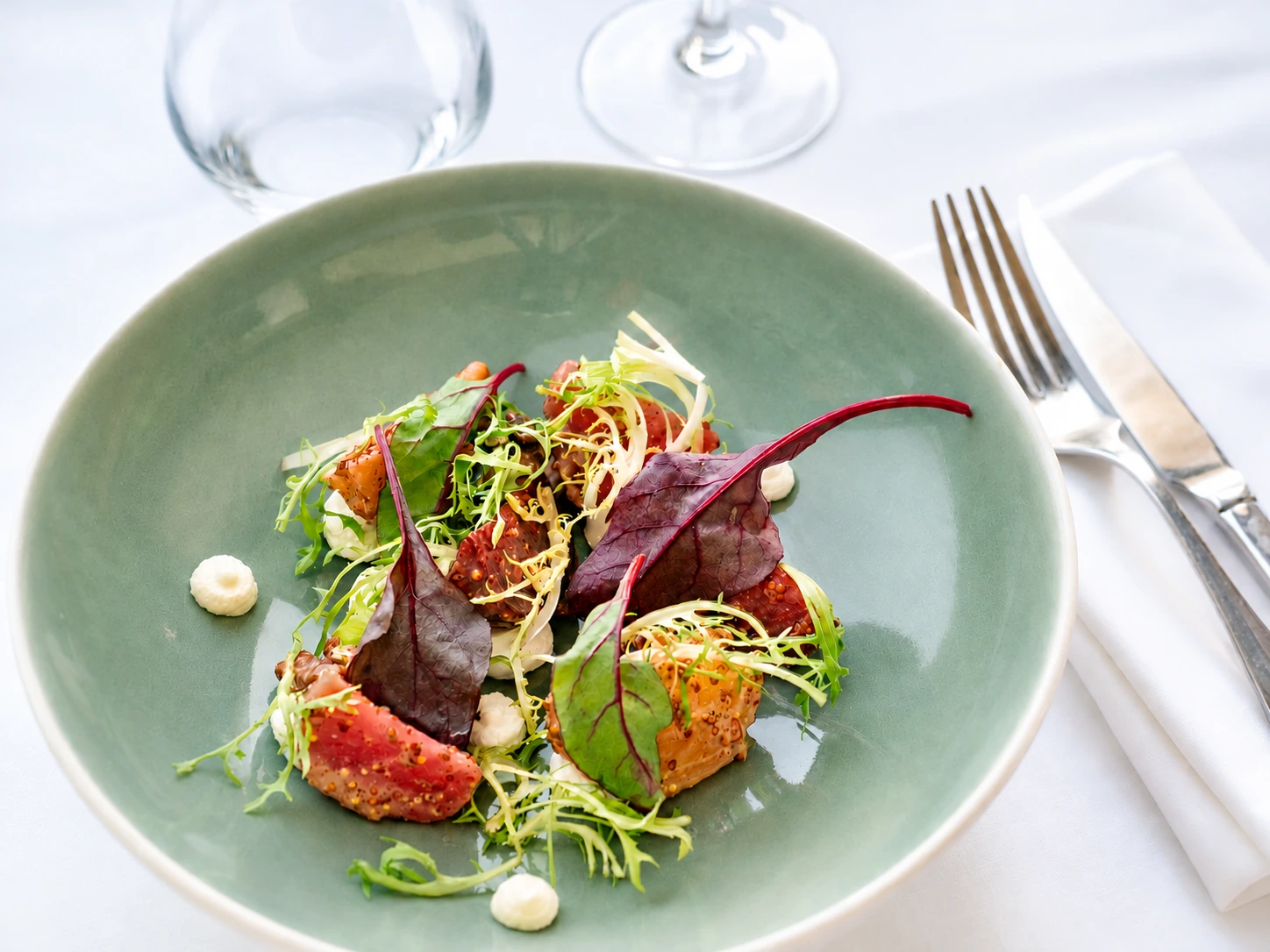 Assiette verte composée de légumes, de figues, de jeunes pousses et de touches de sauce, sur une table dressée